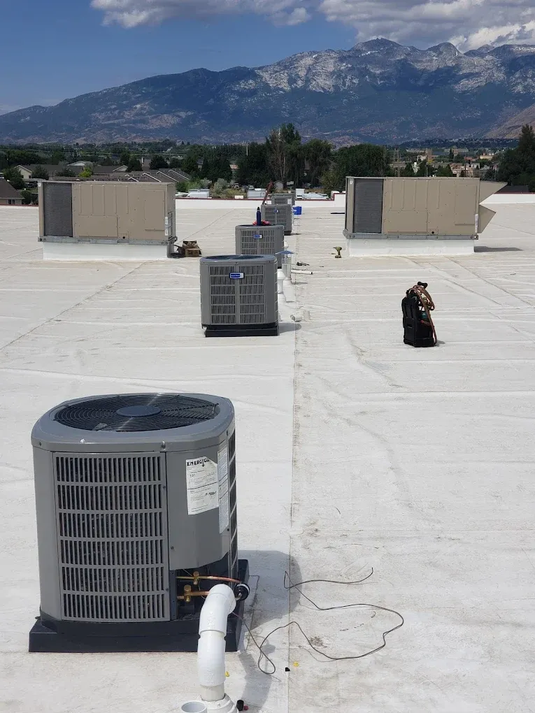 Rooftop view of air conditioning units in a row, with mountains in the background and a sunny sky. JL Mechanical - Heating & Cooling