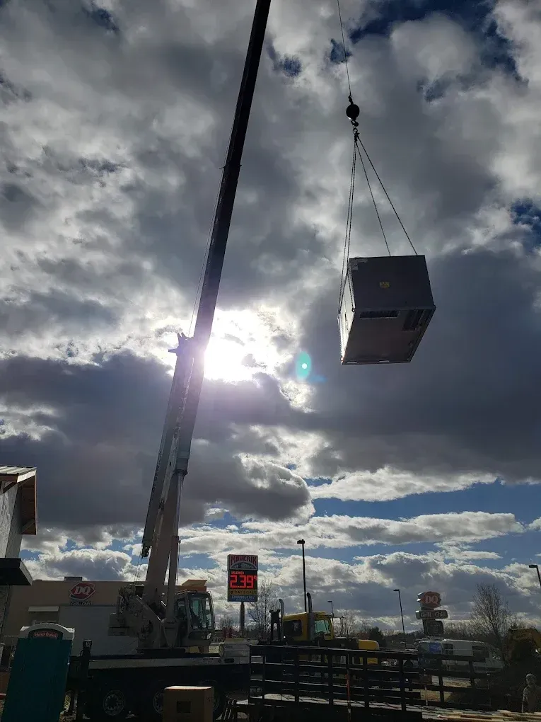 A crane lifting a rectangular object against a cloudy sky. JL Mechanical - Heating & Cooling