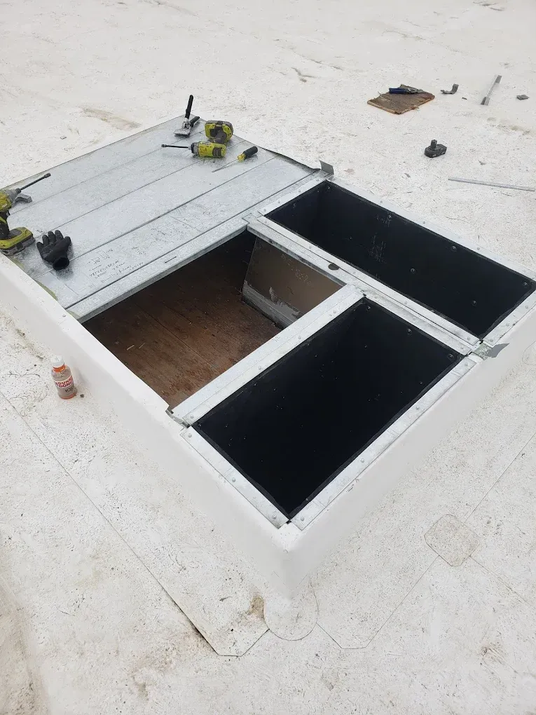 A flat roof with an open skylight being worked on. Metal and wood are visible. JL Mechanical - Heating & Cooling