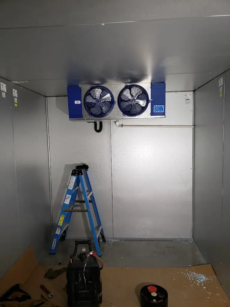Inside a walk-in cooler: blue ladder, fans, door, and equipment on floor. JL Mechanical - Heating & Cooling