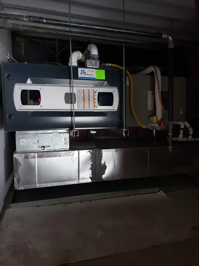 HVAC unit in a utility room. Gray and silver components, ductwork, and piping. JL Mechanical - Heating & Cooling