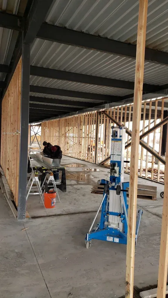 Construction site with wood framing, metal beams, and a blue lift. Workers are present.JL Mechanical - Heating & Cooling