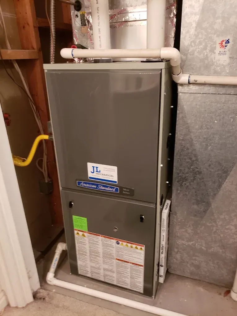 Gray furnace in a utility room with white pipes. JL Mechanical - Heating & Cooling