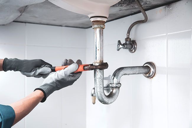 A plumber is fixing a sink pipe with a wrench.