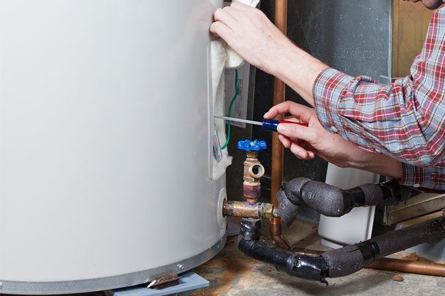 A man is fixing a water heater with a screwdriver.
