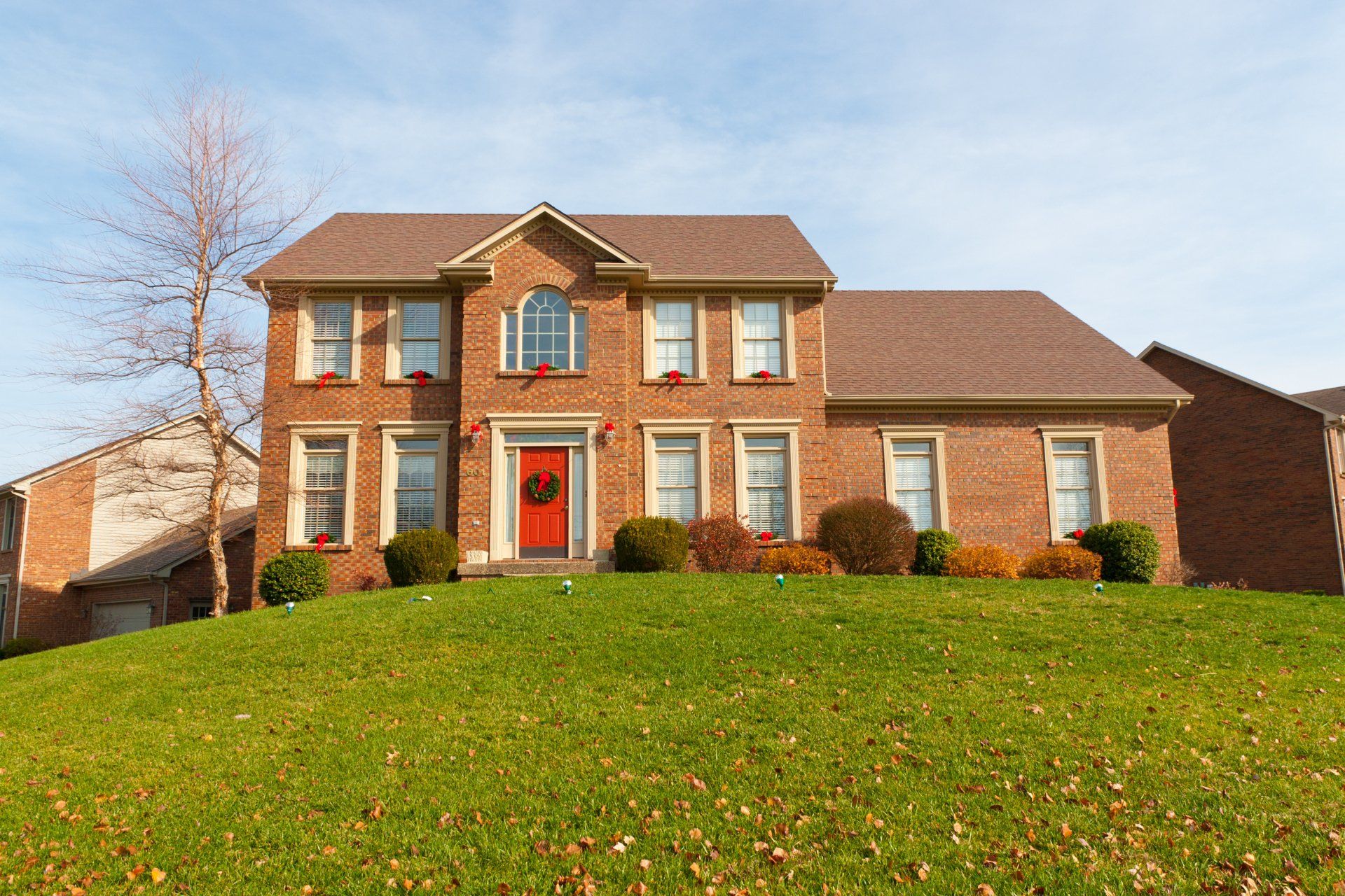 Cape Cod style home with asphalt shingle roof and brick exterior Two-story brick house with gable roofing and red front door in Cape Cod neighborhood
