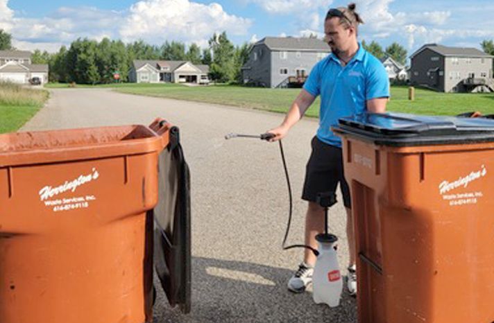 A man is spraying a trash can with a sprayer.