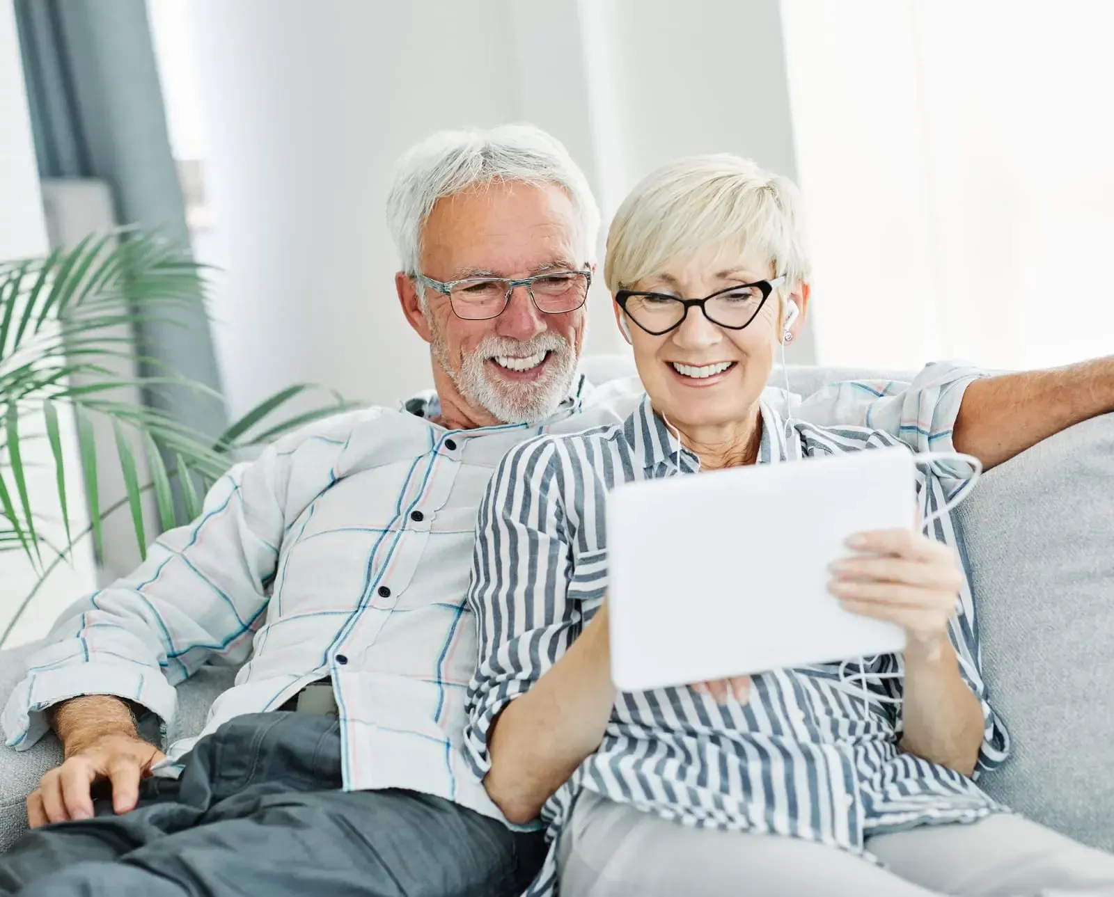 A man and a woman are sitting on a couch looking at a tablet.