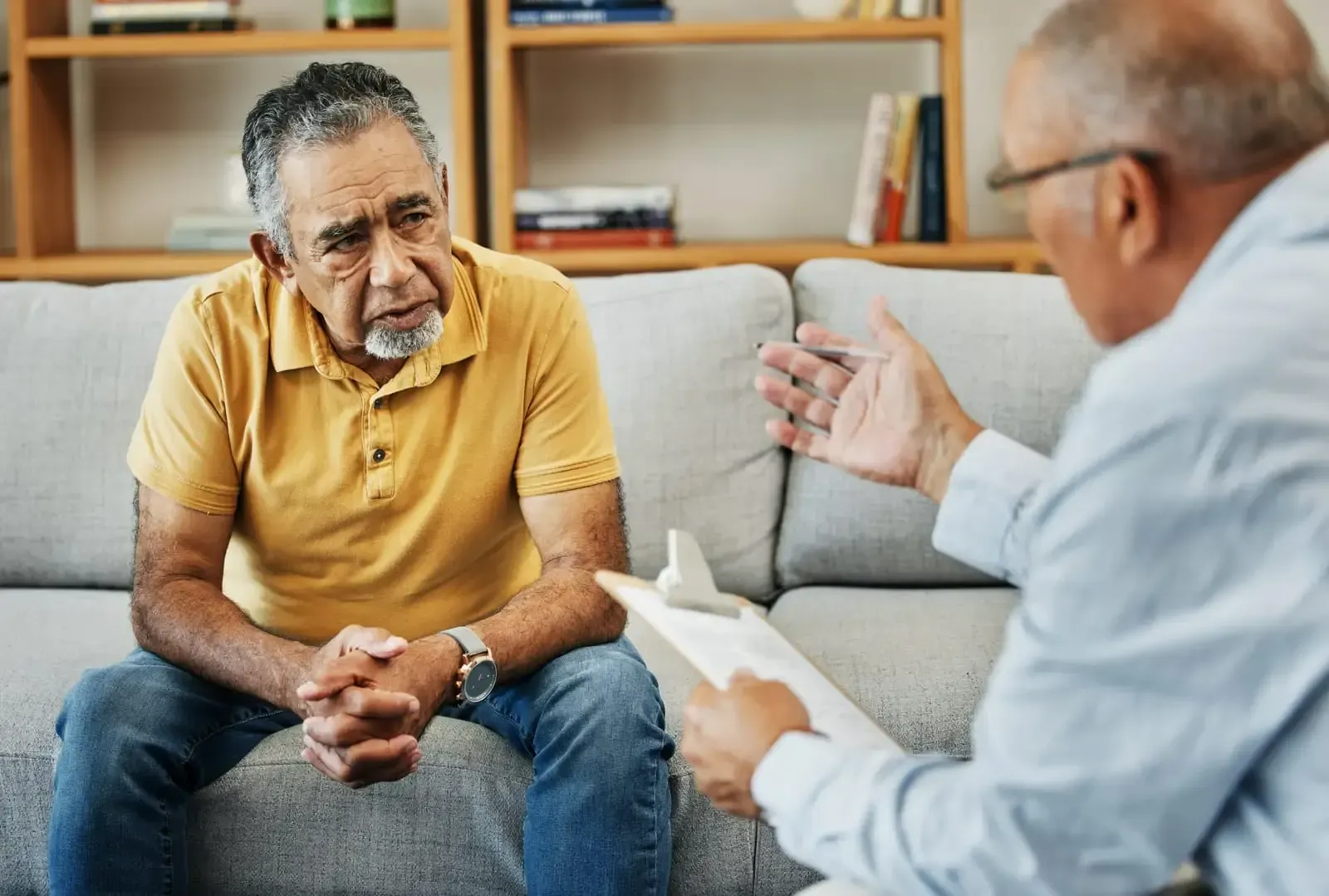 An older man is sitting on a couch talking to a doctor.