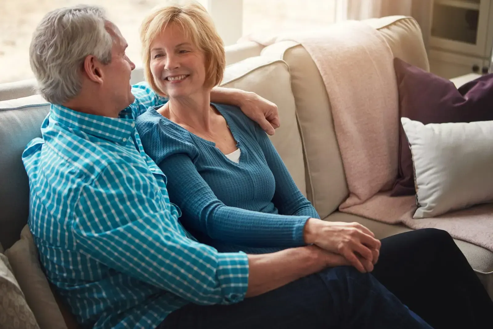 A man and a woman are sitting on a couch holding hands.