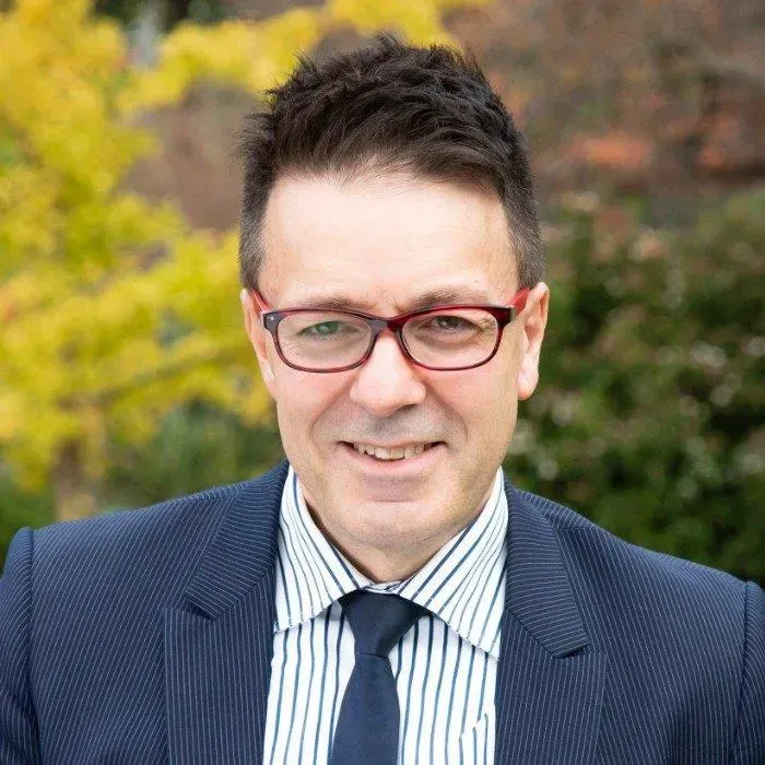 A man wearing glasses and a suit and tie is smiling for the camera.