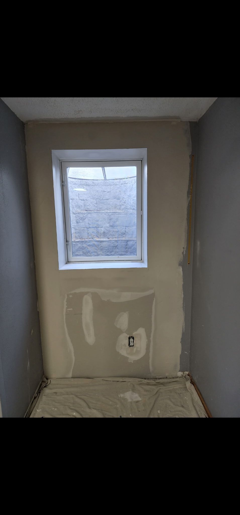 A small room with a window and drywall repair in progress. Gray walls, beige plaster.