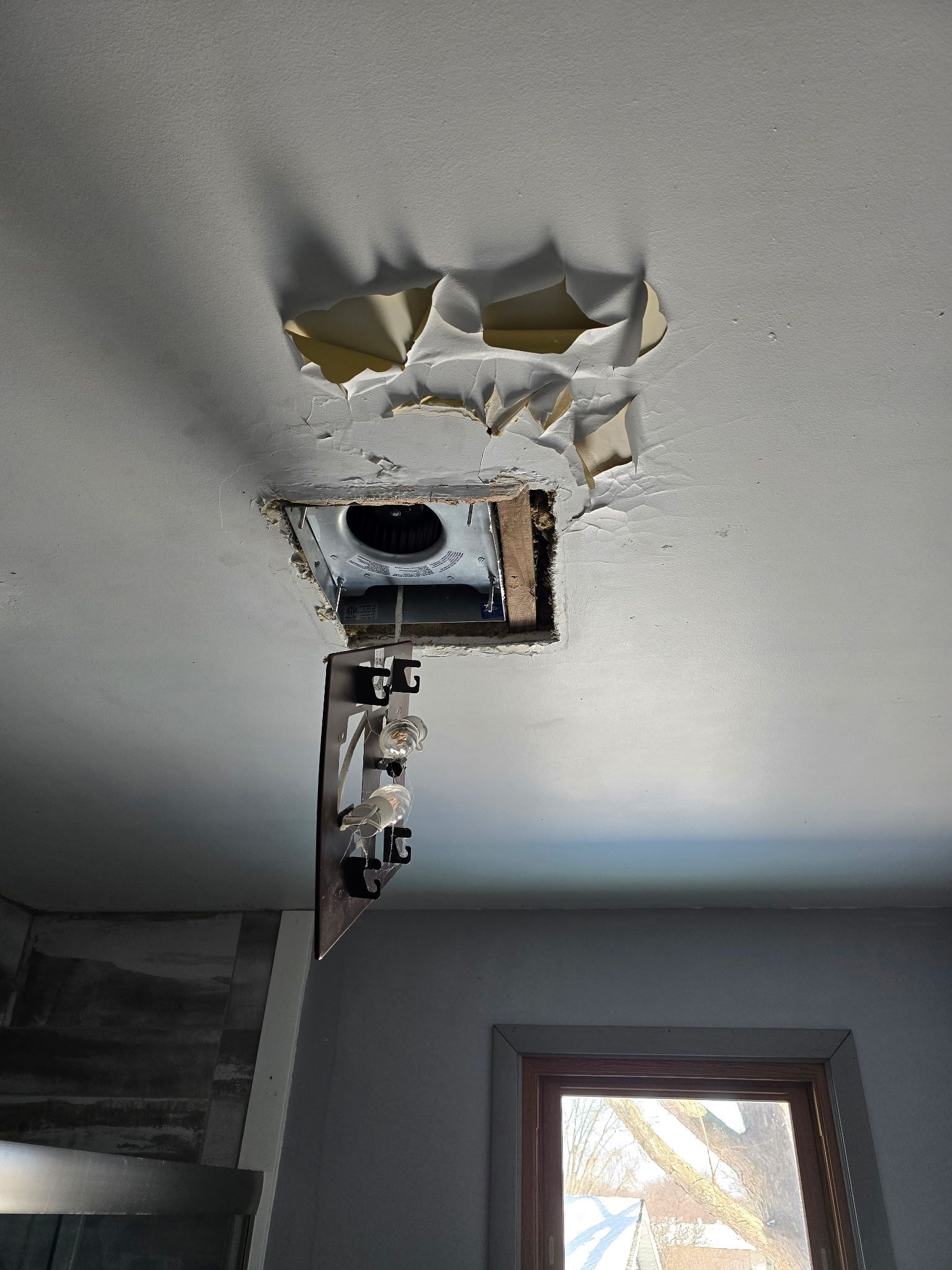 A hole in the ceiling of a room with a window.