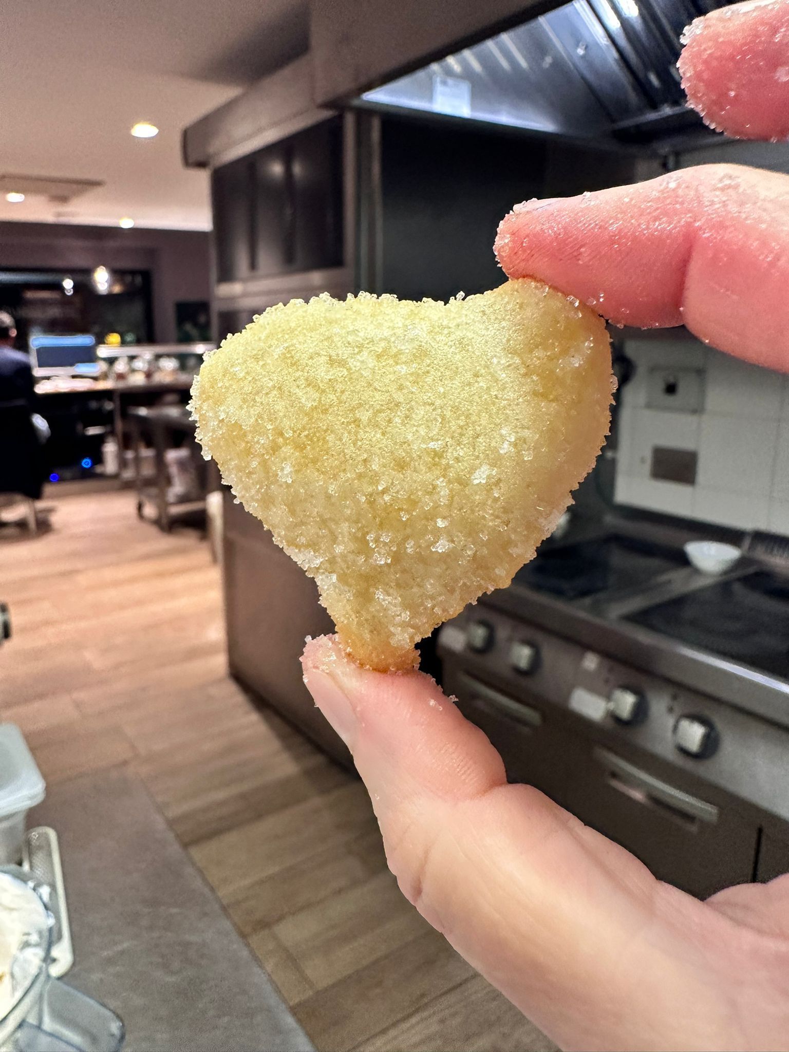 Mano che tiene un alimento fritto dorato a forma di cuore.