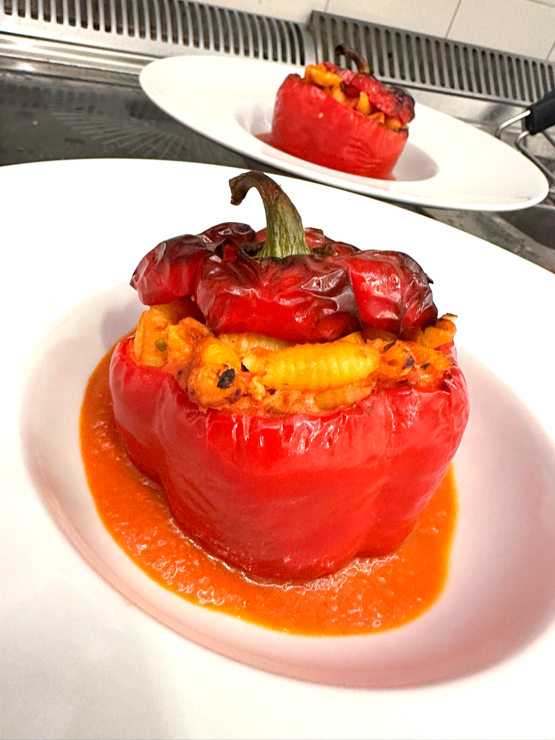 Peperone rosso ripieno su un piatto con salsa all'arancia; un altro sullo sfondo.