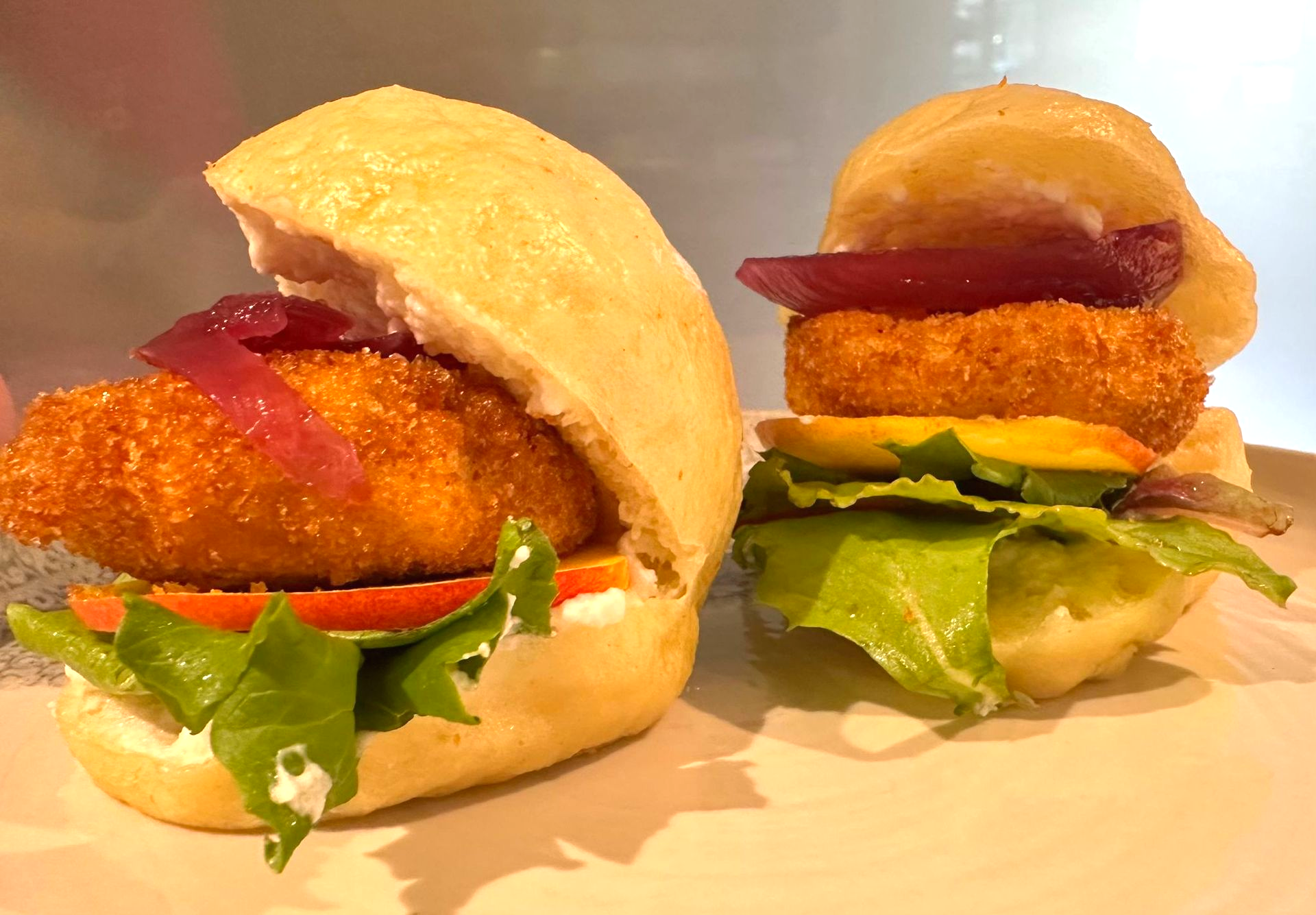 Due mini hamburger su un piatto; ognuno contiene una polpetta fritta, cipolla rossa, pomodoro, lattuga e panino.