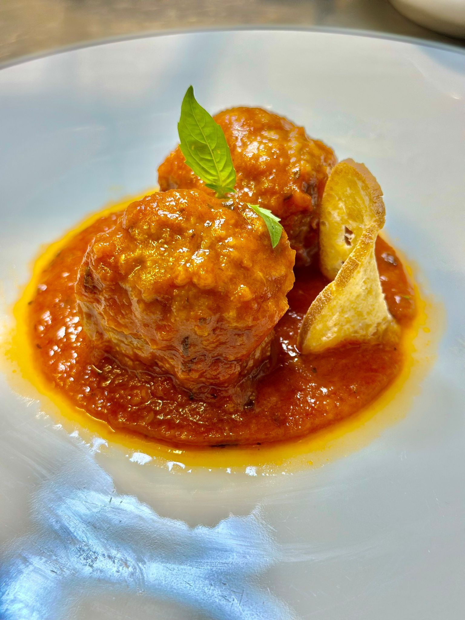 Due polpette in salsa di pomodoro, guarnite con menta e un crostino su un piatto bianco in cucina.
