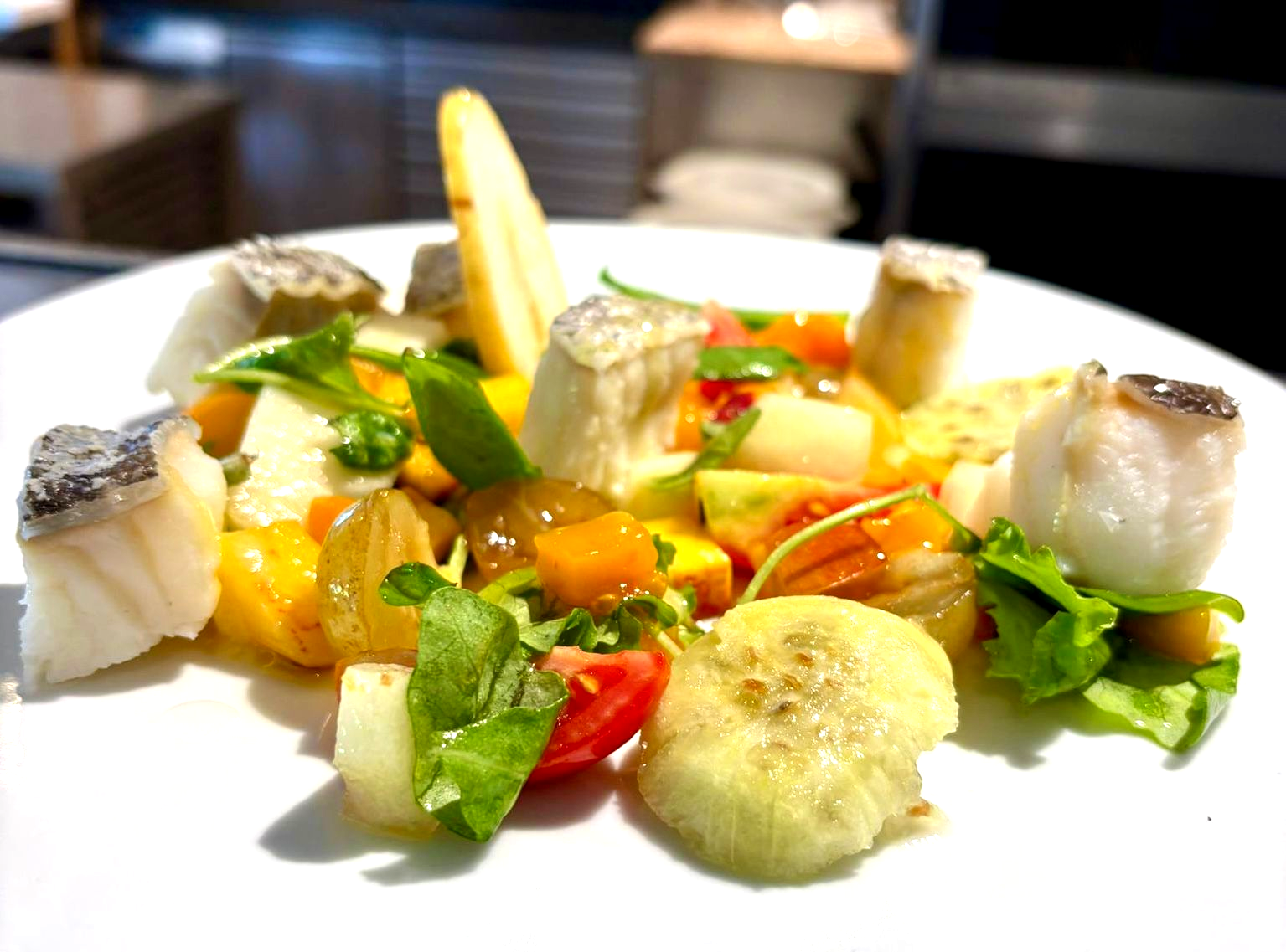 Piatto di cibo colorato con pesce bianco, verdure ed erbe aromatiche.