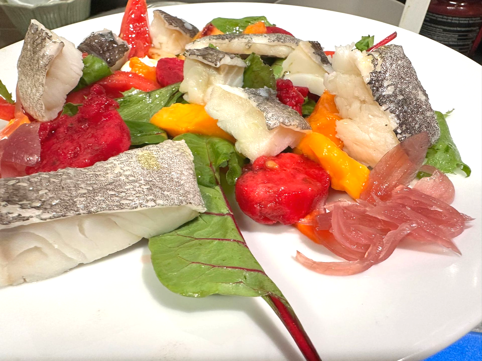 Piatto di insalata con pesce e frutta colorata.