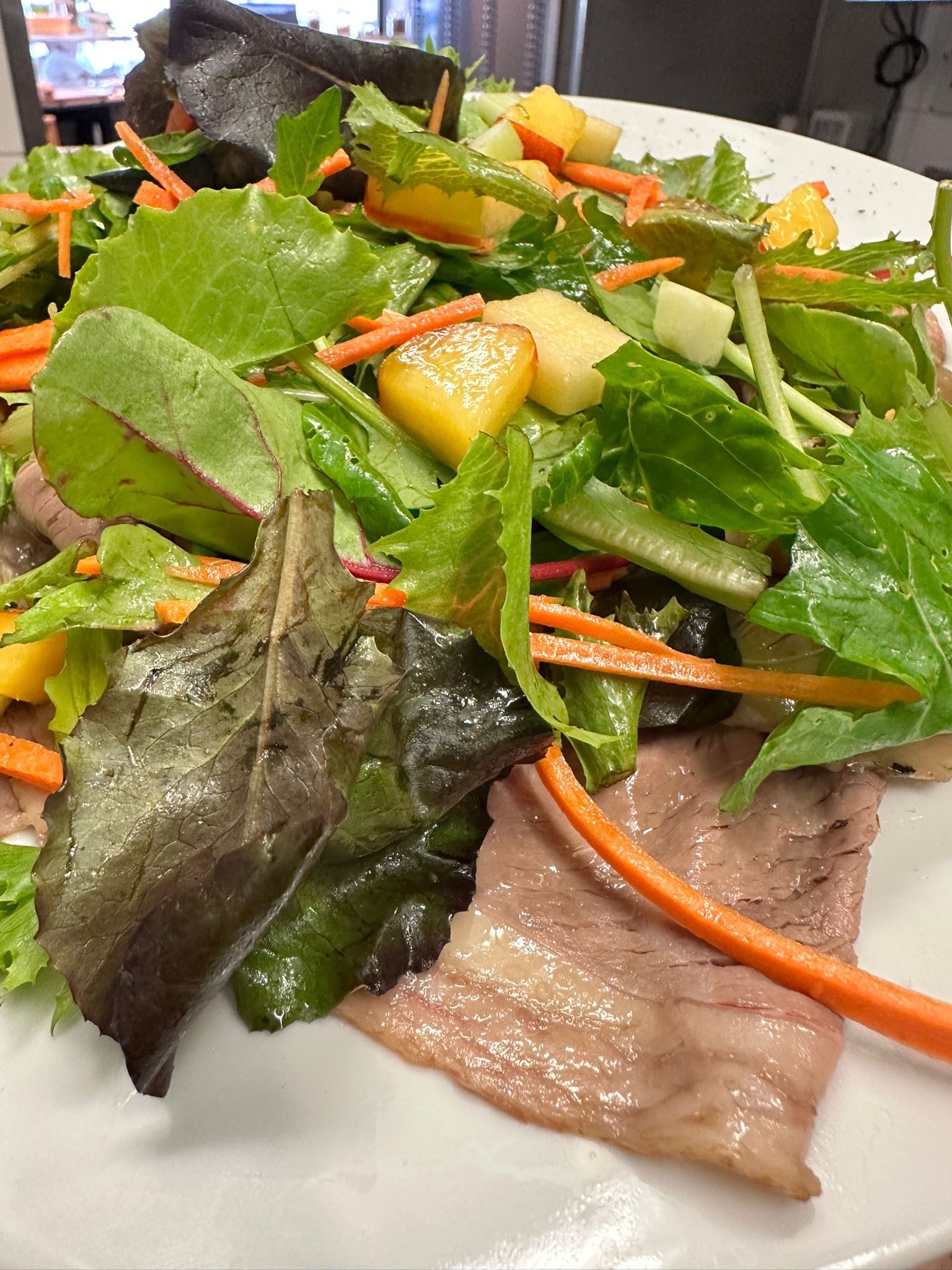 Insalata con verdure, carote, frutta e carne su un piatto bianco.