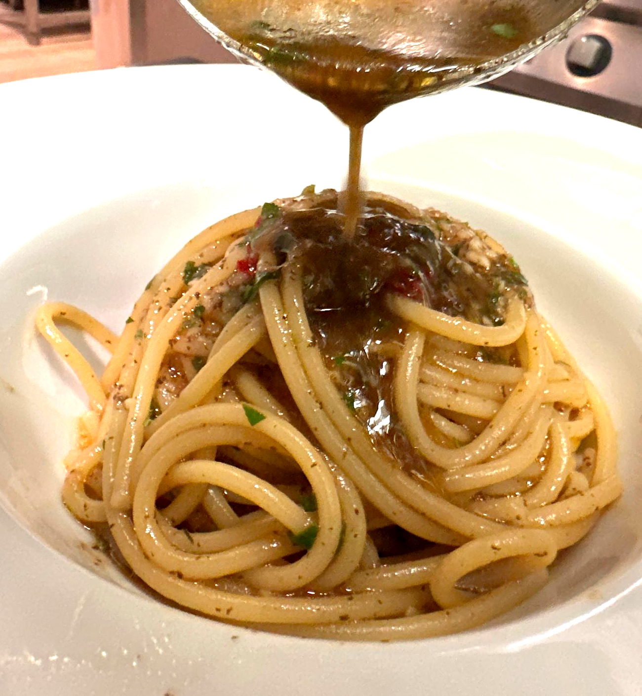 Spaghetti in una ciotola bianca conditi con la salsa preparata con un cucchiaio.