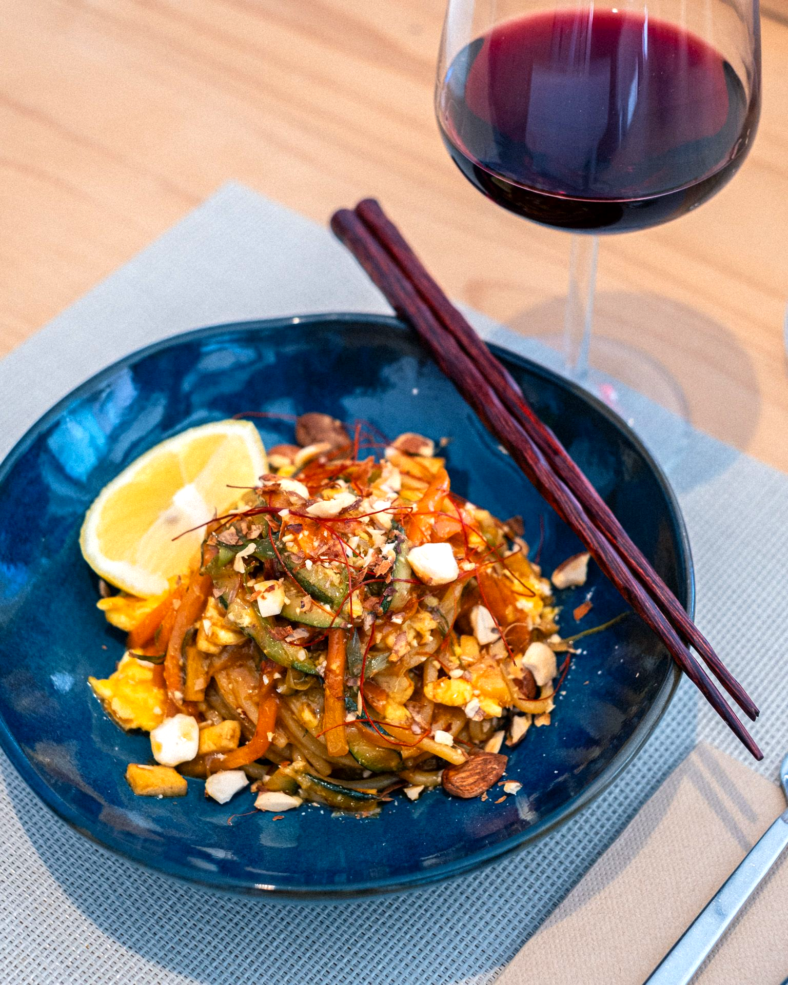 Pad Thai, mandorle, limone, bacchette e vino rosso in una ciotola blu.