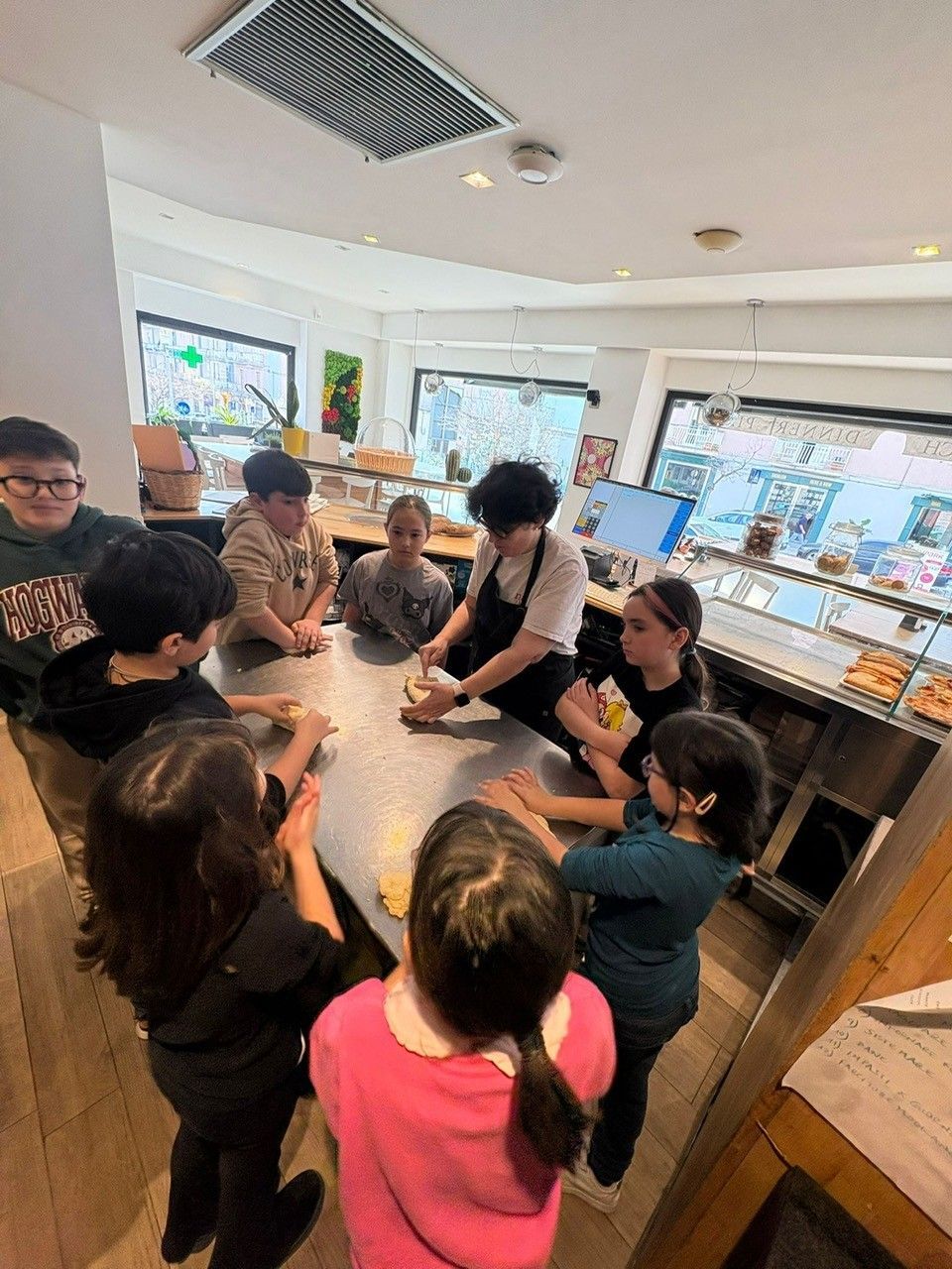 I bambini osservano un fornaio preparare l'impasto in una panetteria, riuniti attorno a un tavolo di acciaio inossidabile.