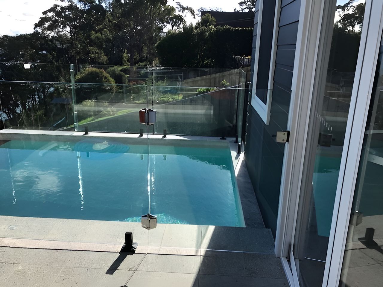 A Swimming Pool With A Glass Fence And A Sliding Glass Door — Master Glass & Glazing In Eleebana, NSW