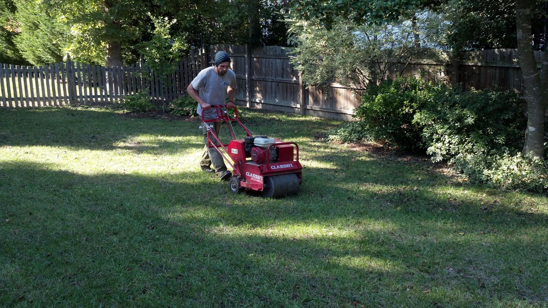 A man is mowing a lush green lawn with a red lawn mower.