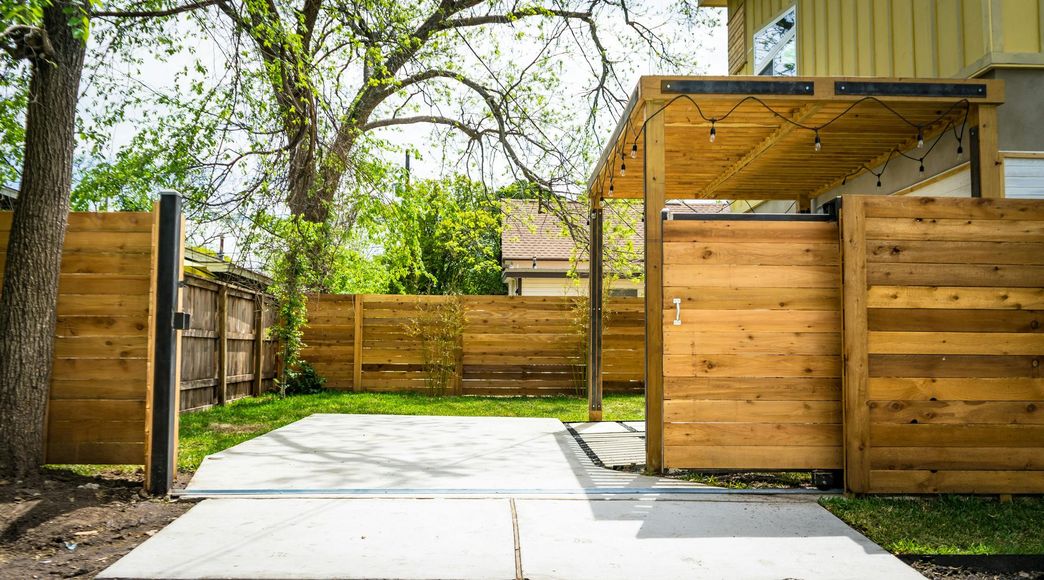 Concrete patio and wooden fences in backyard, with a covered area strung with lights.
