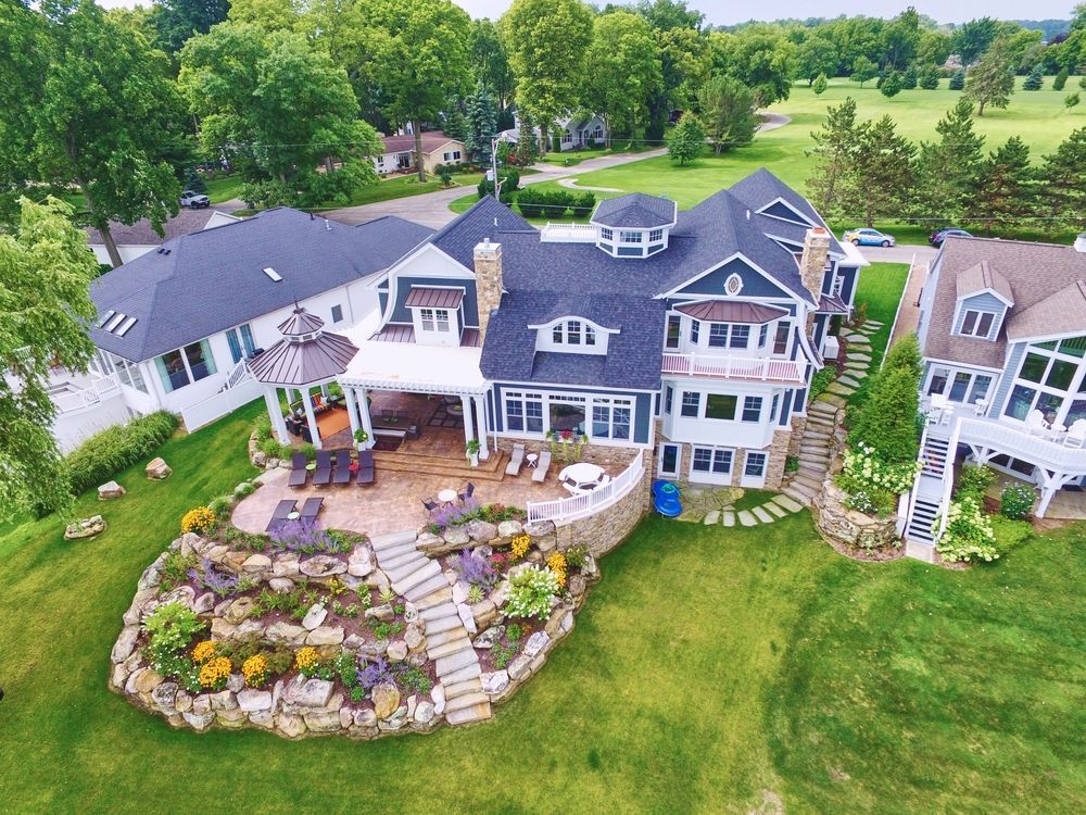 Aerial view of a large, multi-level lake house with a stone patio, landscaping, and a view of a golf course.