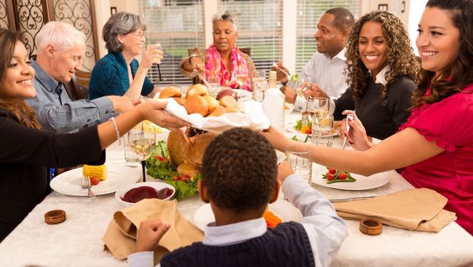 A diverse happy family passes food at a holiday meal.