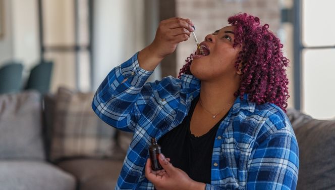 A young woman in a blue plaid shirt drops THC Cannabis tincture under her tongue as a discreet method of consuming weed.