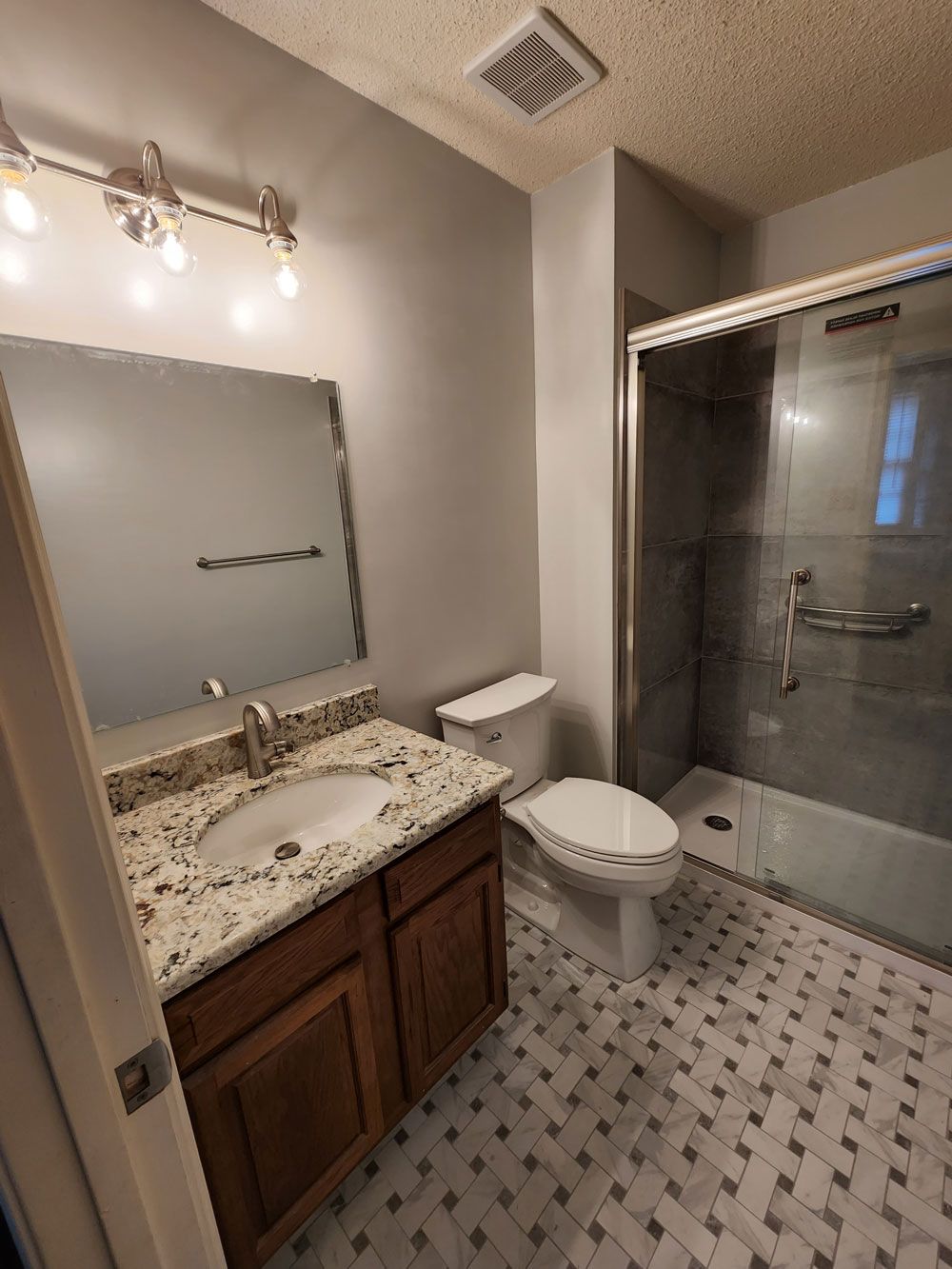 A bathroom with a toilet , sink , mirror and walk in shower.