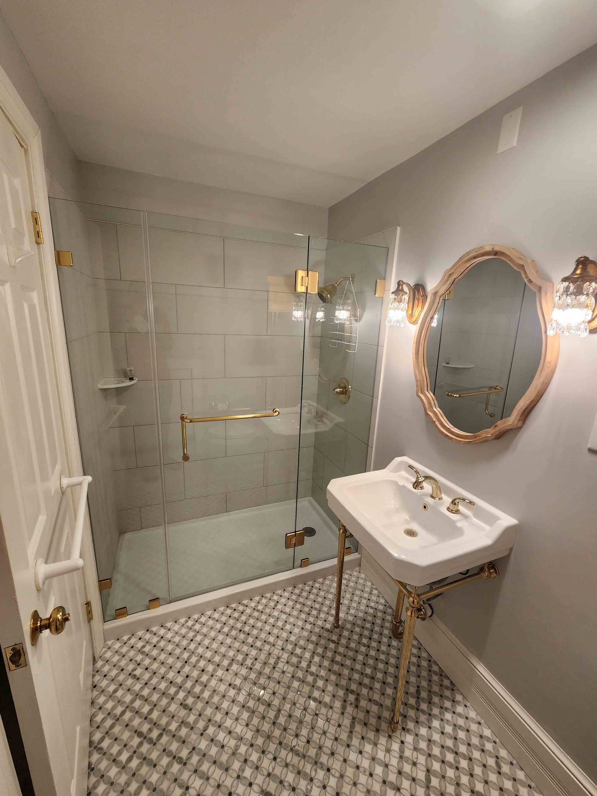 Bathroom with white pedestal sink, glass shower, and gold accents.