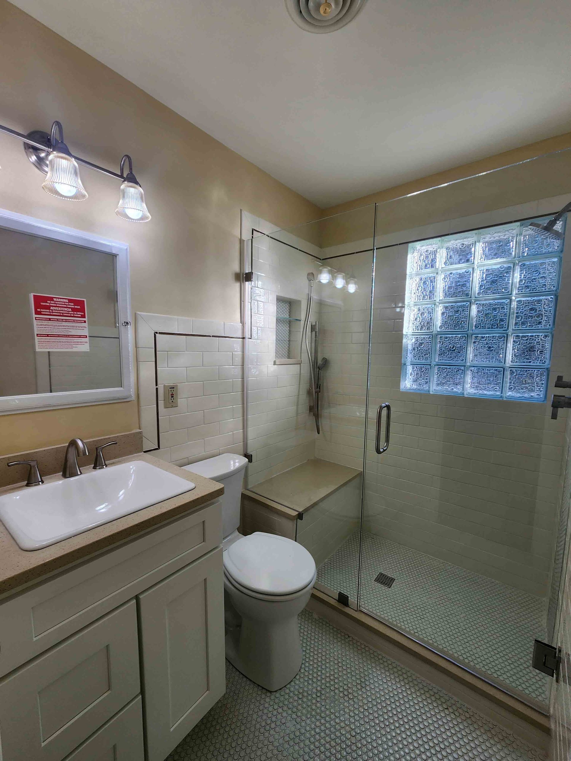A bathroom with a toilet , sink , mirror and walk in shower.