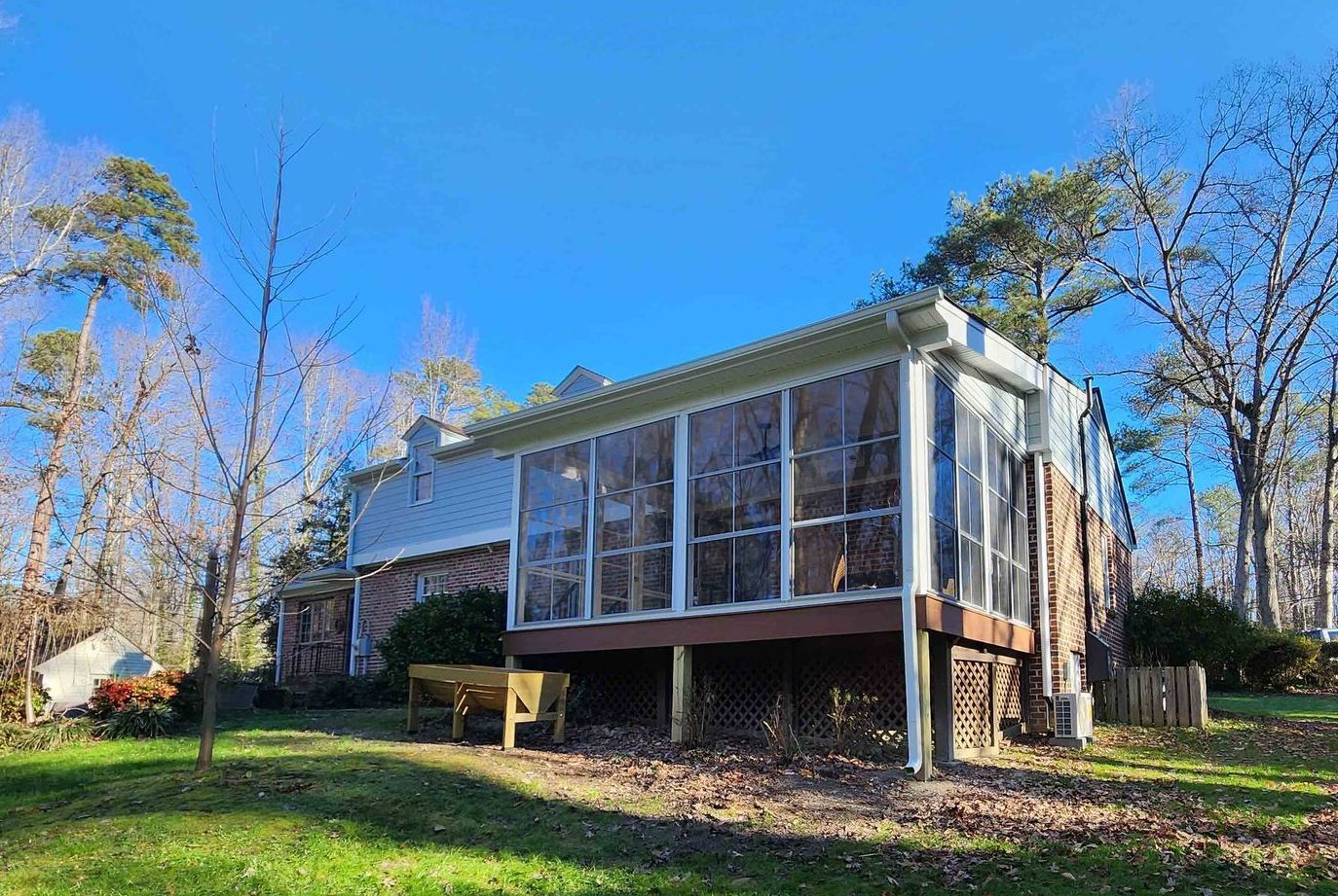 A house with a screened in porch and a bench in front of it.