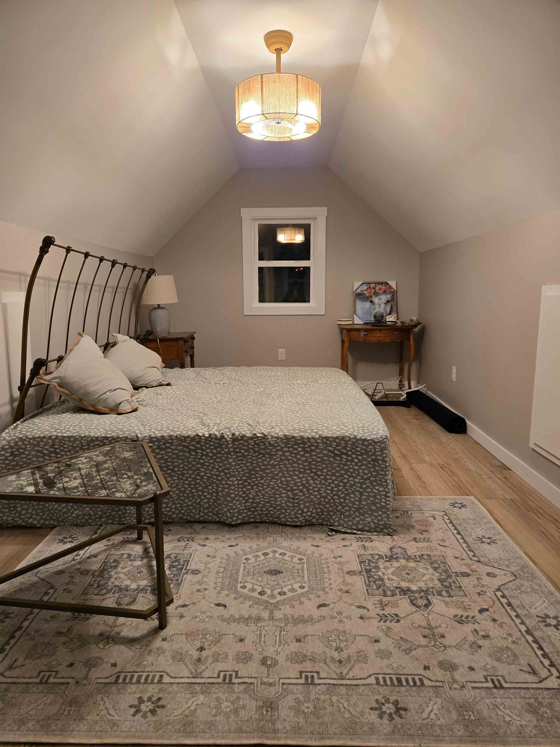 A bedroom with a bed , rug , table and window.