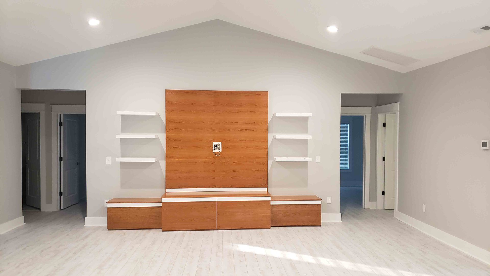 An empty living room with a wooden entertainment center and shelves.
