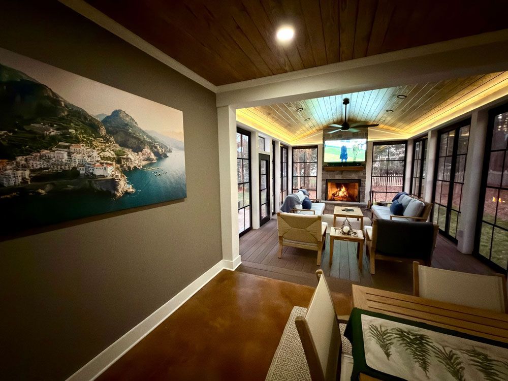 Sunroom with a fireplace, TV, and view of the outdoors. Features furniture and a large landscape photo on the wall.