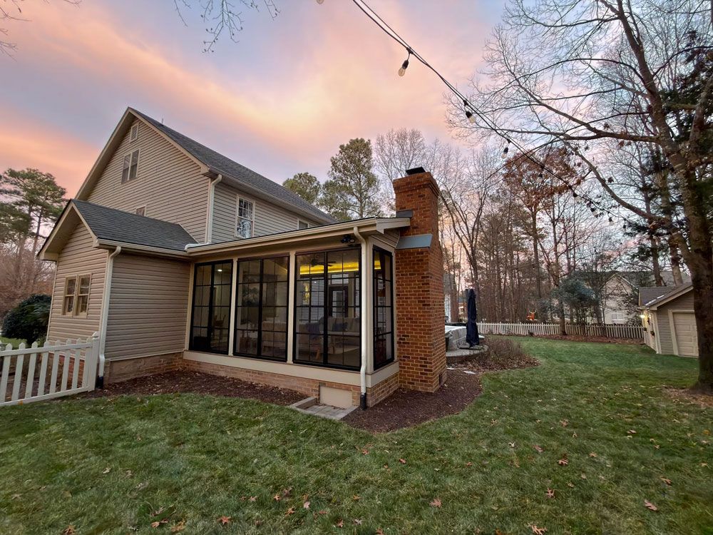 House exterior with sunroom, brick chimney, and colorful sunset sky.