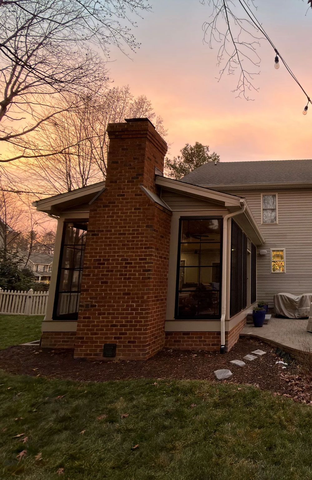 Brick chimney on screened porch, sunset sky.