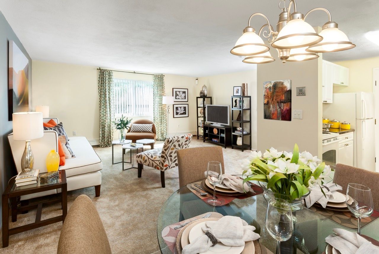 Open-concept apartment living area with sofa, chairs, glass dining table, and visible kitchen.