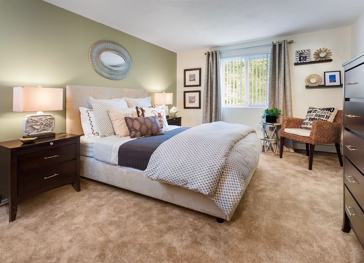 Bedroom in an apartment with a king bed, two nightstands, dresser, and window with curtains.