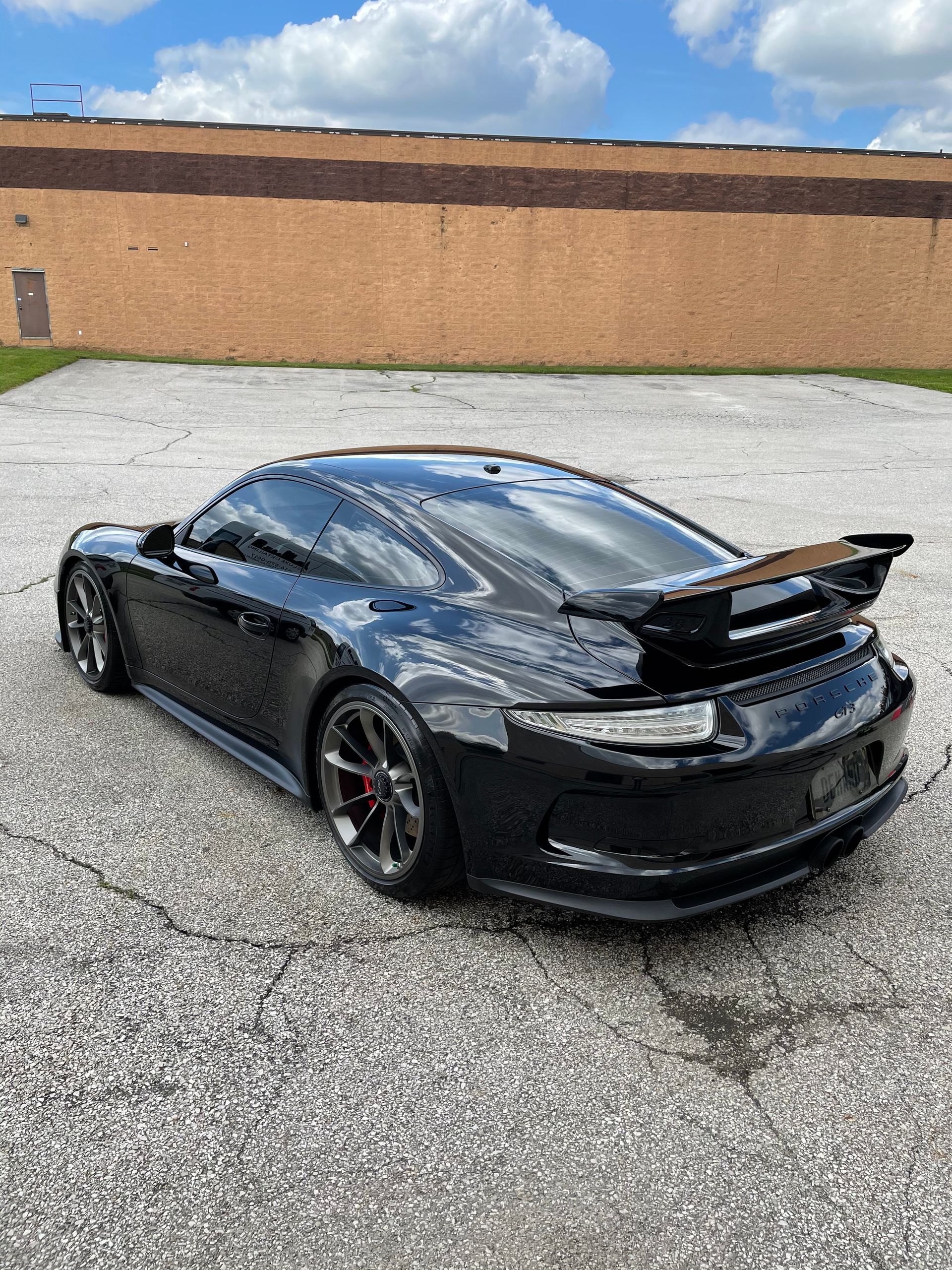 A black porsche 911 gt3 is parked in a parking lot in front of a building.