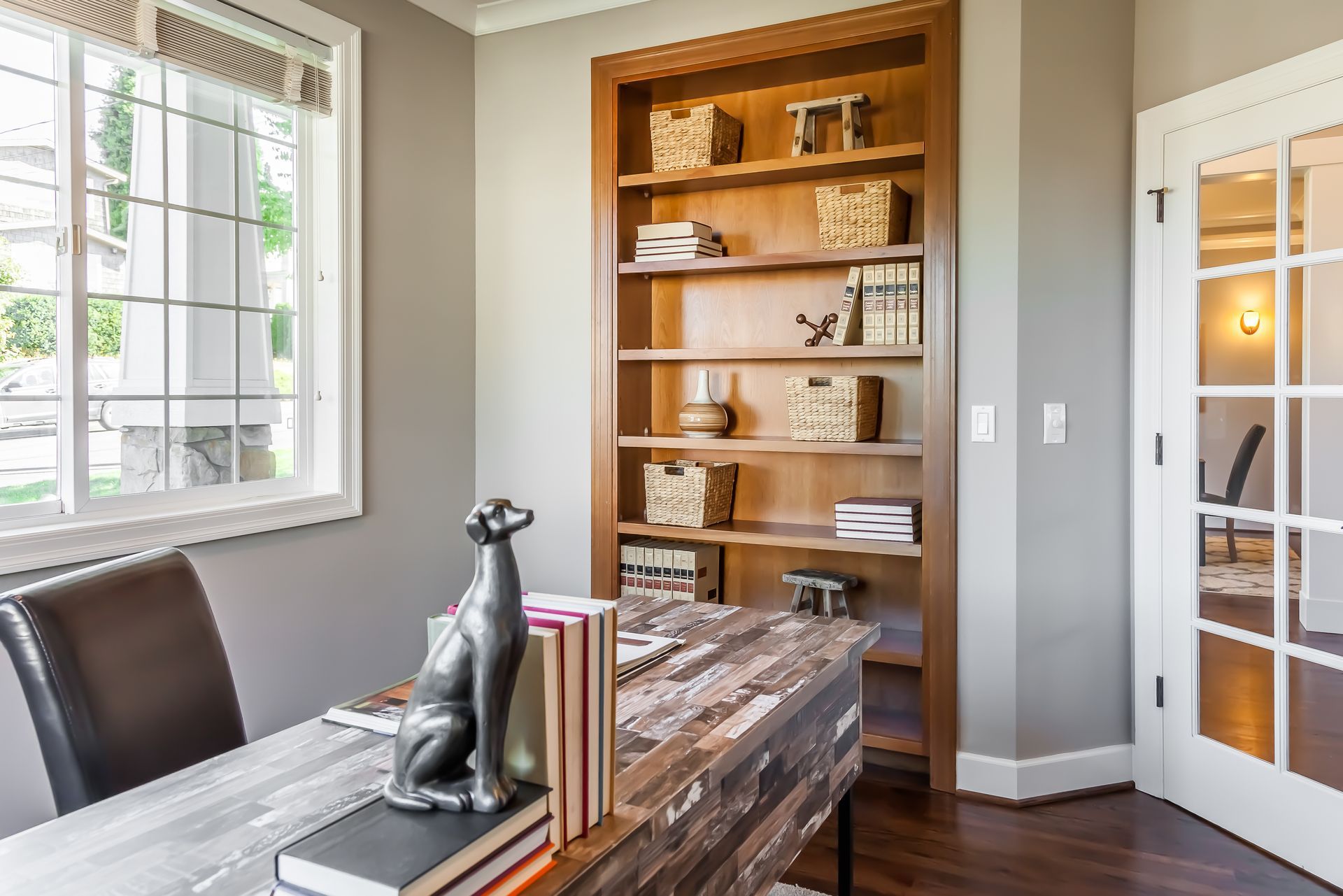 A home office with a desk , chair , bookshelf and window.