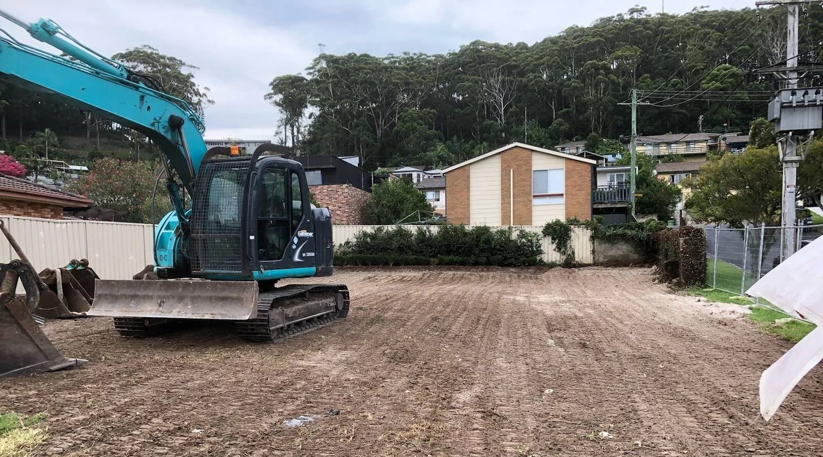 An excavator working on a newly cleared lot. A house is in the background.