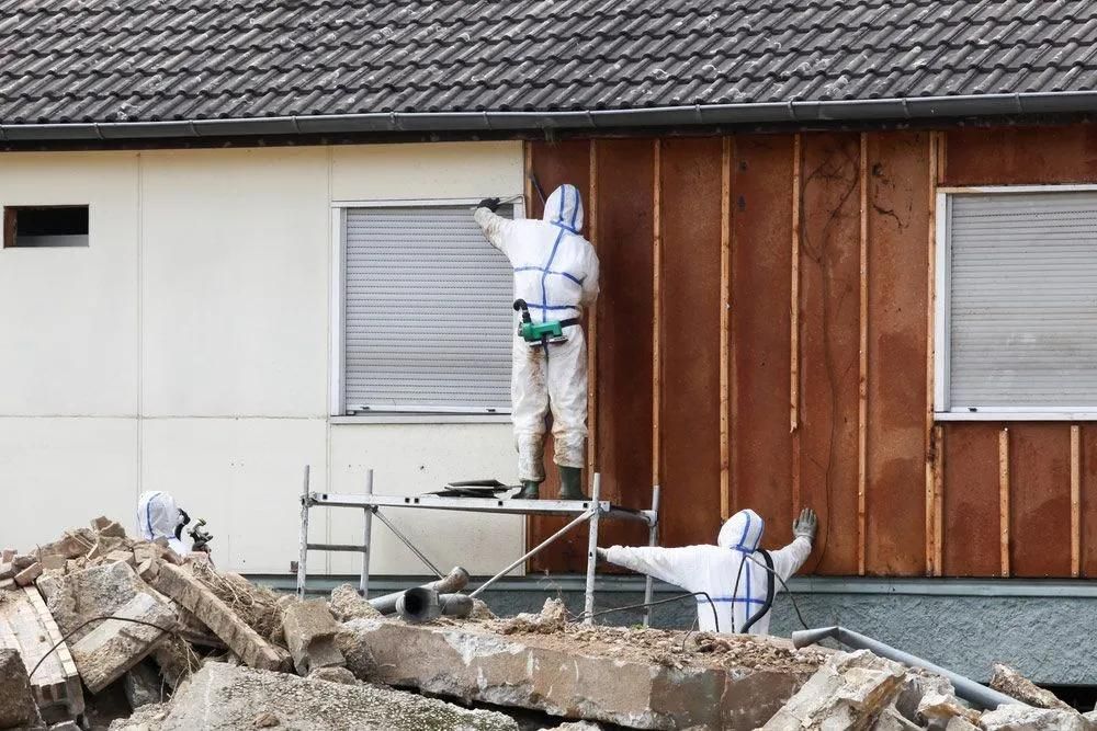 Two Men in Protective Suits Are Working on The Side of A House — Central Coast Complete Demolition &