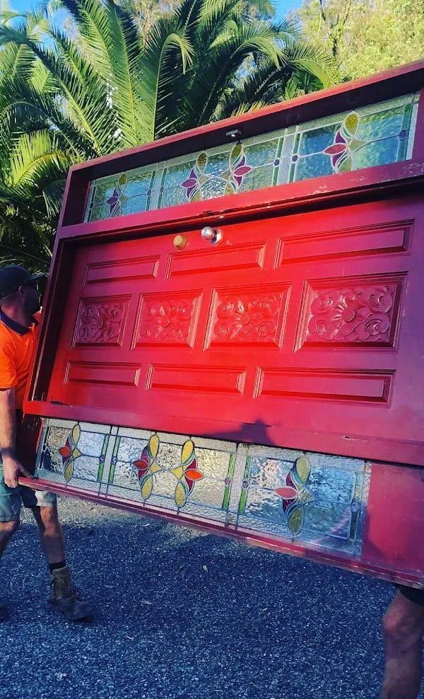 Two men carrying a large red door with stained glass — Central Coast Complete Demolition & Tree Service in Buff Point, NSW