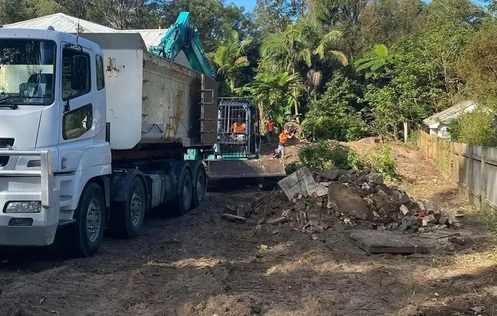 A Dump Truck Is Driving Down a Dirt Road Next to A Construction Site — Central Coast Complete Demolition & Tree Service in Buff Point, NSW